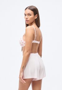Bralette rose clair avec motifs de cœurs rouges, bretelles fines et fermeture au dos, associé à un short rose transparent présentant un design texturé.