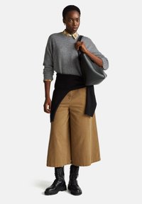 Šedý pletený svetr s černým obalem, límeček z kostkované košile. Své volné kalhoty v tělové barvě a černé šněrovací boty. Jednoduchá černá kabelka.