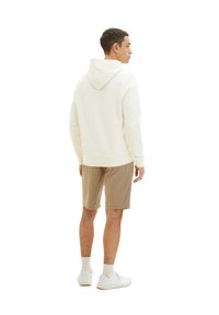 Hellbeige Kapuzenpullover mit Kapuze, gerippten Bündchen und lockerer Passform, kombiniert mit beigen Shorts und weißen Sneakern, aus der Rückansicht betrachtet.