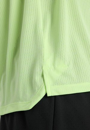 Tissu vert clair perforé superposé à un tissu noir perforé, montrant un ourlet et une fente latérale sur le vêtement.