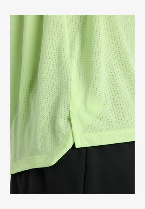 Tissu vert clair perforé superposé à un tissu noir perforé, montrant un ourlet et une fente latérale sur le vêtement.