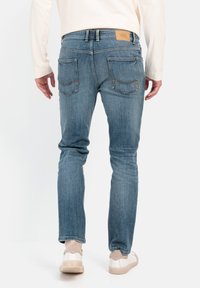 Blå denimjeans i slim fit med baglommer og et læderlabel i taljen, båret med hvide sneakers og en lys skjorte.