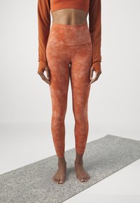 High-waisted, orange tie-dye leggings with a smooth, stretchy texture and seamless design, paired with a matching crop top.