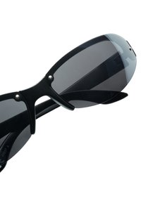 Mustat aurinkolasit, joissa on kaareva muotoilu, tummat linssit ja matta pinta, joita korostavat hopeiset yksityiskohdat nenäpuomissa ja templeissa.