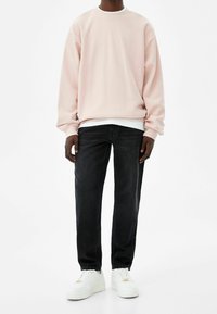 Vaaleanpunainen collegepaita pyöreällä kaula-aukolla ja laskostetuilla olkapäillä, yhdistetty tummansinisiin farkkuihin ja valkoisiin lenkkareihin. Pinta teksturoitu, rento istuvuus.