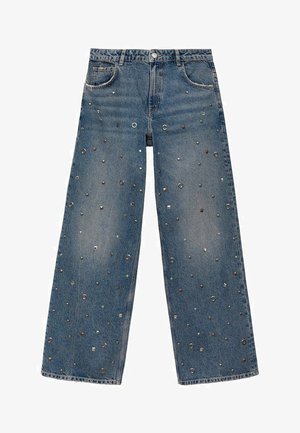 Weite Denim-Jeans in Hellblau, mit metallischen Nieten und kreisförmigen Akzenten über den Stoff verteilt, um zusätzliche Textur und Detail zu bieten.
