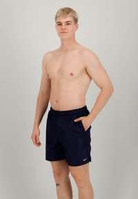 Pantaloni da bagno blu navy con elastico in vita e tasche, con il logo bianco di Nike sulla gamba sinistra. Tessuto liscio e leggero.