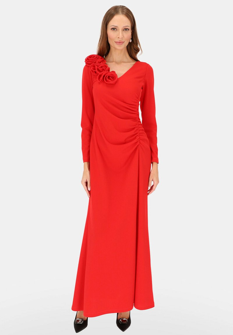 Długa czerwona sukienka z długimi rękawami, ozdobiona drapowanym wzorem oraz trójwymiarowym kwiatem na lewym ramieniu, gładka faktura materiału.