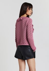 Maglione lavorato a maglia rosa con un motivo a diamante testurizzato e colletto a volant, abbinato a pantaloni corti in pelle nera.