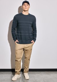Navy striped knit sweater, beige chinos, and light-colored sneakers. Casual fit with ribbed cuffs and waistband. Smooth texture, no patterns.