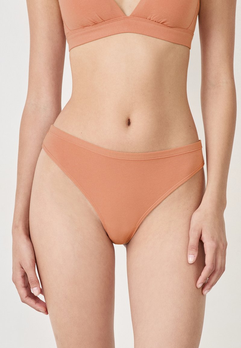 Bikini w kolorze brzoskwiniowym o gładkiej fakturze, z wysokim krojem nogawki i szerokim pasem w talii. Prosty fason bez widocznych wzorów czy akcentów.