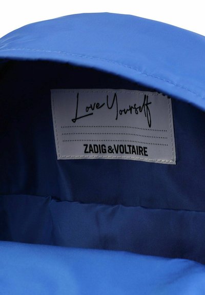 Tissu intérieur bleu avec une texture lisse, comportant une étiquette de vêtement qui indique "Aime-toi" et "ZADIG & VOLTAIRE" en texte noir.