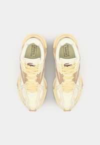 Baskets Lacoste de couleur jaune clair, avec des accents beige, un dessus texturé, mettant en avant un laçage proéminent et un logo sur la languette.