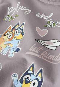 Šedá bavlněná látka zdobí kreslené ilustrace dvou psů, kteří se objímají a jsou obklopeni květinami, srdcem a textem "nejlepší přátelé".