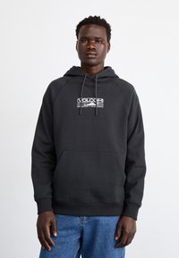 Fekete kapucnis pulóver zsinórral, elülső zsebbel és Volcom logónyomattal. A szövet puha, sima tapintású. Normál szabás és bordázott mandzsetták.