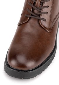 Hnědé kožené boty s hladkým povrchem, kulatou špičkou a černou gumovou podrážkou. Šněrování je tmavě hnědé a design obsahuje jemné švy.