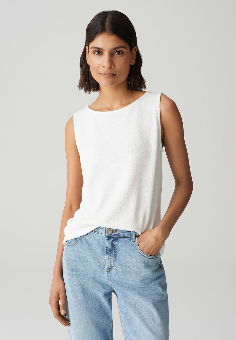 Haut sans manches blanc en tissu texturé, avec un col rond et une coupe décontractée, associé à un jean en denim bleu clair.