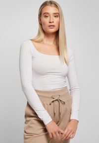 Hvitt langermet topp med firkantet utringning, kombinert med beige joggebukser med elastisk liv og snor.