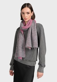 Écharpe grise avec un tissage texturé et des accents à rayures roses, drapée doucement autour du cou. Portée avec un sweat-shirt gris.