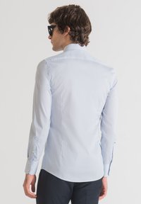 Camisa de manga larga azul claro en un diseño ajustado, hecha de una tela suave con detalles de botones en los puños y la parte trasera. Vista desde atrás.