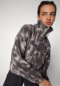 Pullover in pile grigio con motivo camouflage, dotato di chiusura con mezza zip e colletto alto. Tessuto leggero e strutturato.