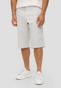 Shorts en coton gris clair avec une coupe décontractée, arrivant au genou, avec une ceinture plate et des poches latérales, associés à des baskets blanches à semelle basse.