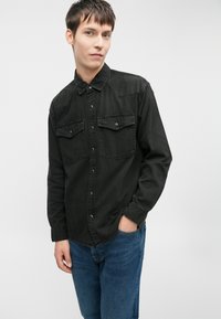 Svart denimskjorte med to brystlommer, trykknapper og spiss krage. Brukes med blå jeans som har en avslappet passform og rette ben.