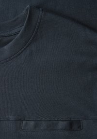 Tmavě námořnicky modré tričko s kulatým výstřihem a hladkou, lehce texturovanou látkou. Na hrudi je vodorovná náprsní kapsa.