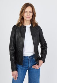 Svart läderjacka med en figursydd design, ståkrage och dragkedjestängning. Detaljer inkluderar stickade axelaccenter och sidofickor.