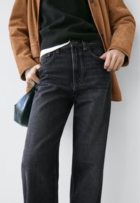 Černé džíny s rovnými nohavicemi, s světlejším šitím a klasickým designem s pěti kapsami. Kombinovány s hnědou semišovou bundou a malou kabelkou.