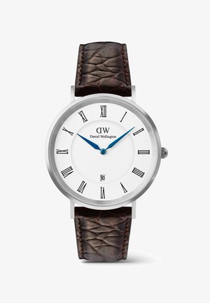Okrągły srebrny zegarek z białą tarczą, czarnymi rzymskimi cyframi, niebieskimi wskazówkami godzinową i minutową, okienkiem daty na godzinie 6 oraz teksturowanym ciemnobrązowym paskiem ze skóry.