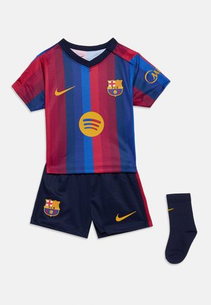 Σετ ποδοσφαίρου παιδικό FC Barcelona με κόκκινη και μπλε ριγέ φανέλα, σκούρα μπλε σορτς και σκούρα μπλε κάλτσες, όλα με τα λογότυπα του συλλόγου και της Nike.