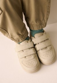 Beiget mokkanahkaiset kengät, joissa on kaksi säädettävää Tarranauhaa ja kärjessä rei'ityksiä, yhdistettynä käännettyihin khakihousuihin ja teelisiin sukkiin.