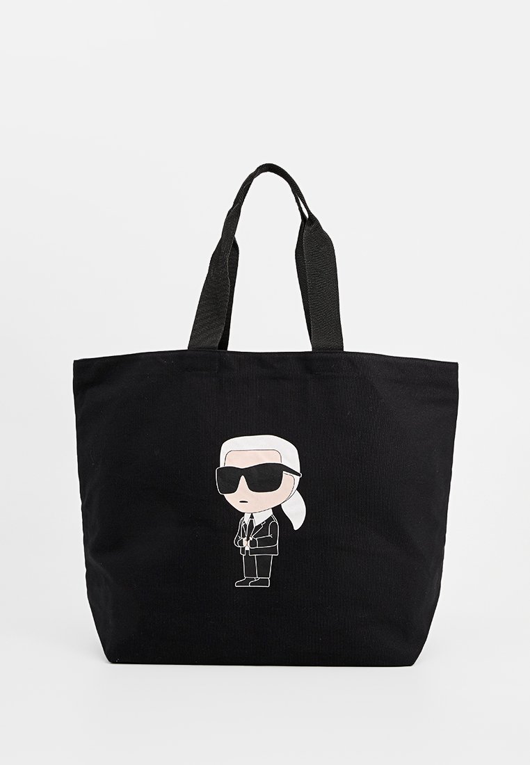 Bolso tote negro hecho de lona, con una figura de dibujos animados que lleva gafas de sol y un traje en la parte frontal. Asas negras resistentes para llevar.