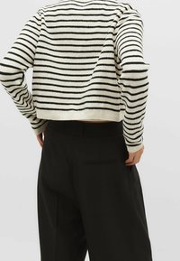 Black and white striped sweater with long sleeves, ribbed hem, and cropped design, paired with high-waisted black trousers featuring a back pocket.