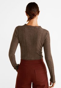 Ruskea pitkähihainen paita, joka on valmistettu pehmeästä materiaalista, ja siinä on muotoiltu design, jossa on pystysaumat. Yhdistetty korkeavyötäröisiin viininpunaisiin housuihin.