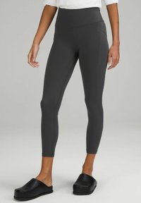 Wysokie, ciemnoszare legginsy wykonane z elastycznej tkaniny, z szwami bocznymi i długością do kostek. W połączeniu z czarnymi klapkami na slip-on.
