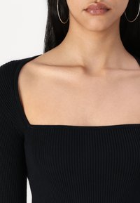 Black ribbed long-sleeve top featuring a square neckline and fitted design. Accentuated by a textured fabric and smooth neckline.