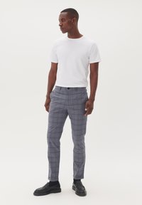 Camiseta blanca de manga corta combinada con pantalones de cuadros gris a medida. Los pantalones cuentan con un cierre de botón y un diseño ajustado con una textura suave.