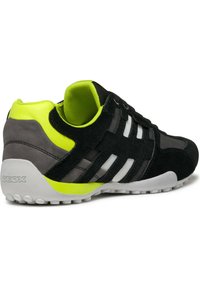 Schwarzer und grauer Sneaker aus Wildleder, mit transparenten Akzenten, neon-grünen Highlights und einer Gummisohle. Logo auf der Ferse sichtbar.