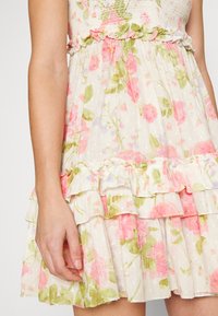Blumenkleid aus einem leichten, strukturierten Stoff mit rosa und grünen Rosen, gestuften Rüschen am Saum und einem gerafften Oberteil.