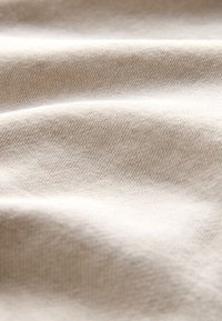 Beiger Stoff mit feiner diagonaler Webstruktur, dargestellt in sanften Falten und natürlichen Licht- und Schattenspielen.