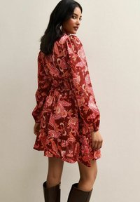 Robe à motifs rouges avec des manches longues et un ourlet roulé, présentant des motifs cachemire en rose et blanc. Texture de tissu lisse.
