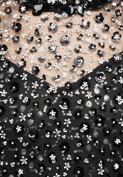 Broderie de sequins et perles florale en noir et blanc sur tissu transparent avec un vêtement noir visible en bas.