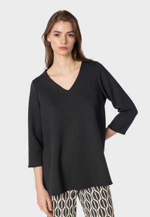 Zwarte V-hals top met 3/4 mouwen, gemaakt van zachte stof, gecombineerd met gemusterde crèmekleurige en zwarte broek met een ovale print.