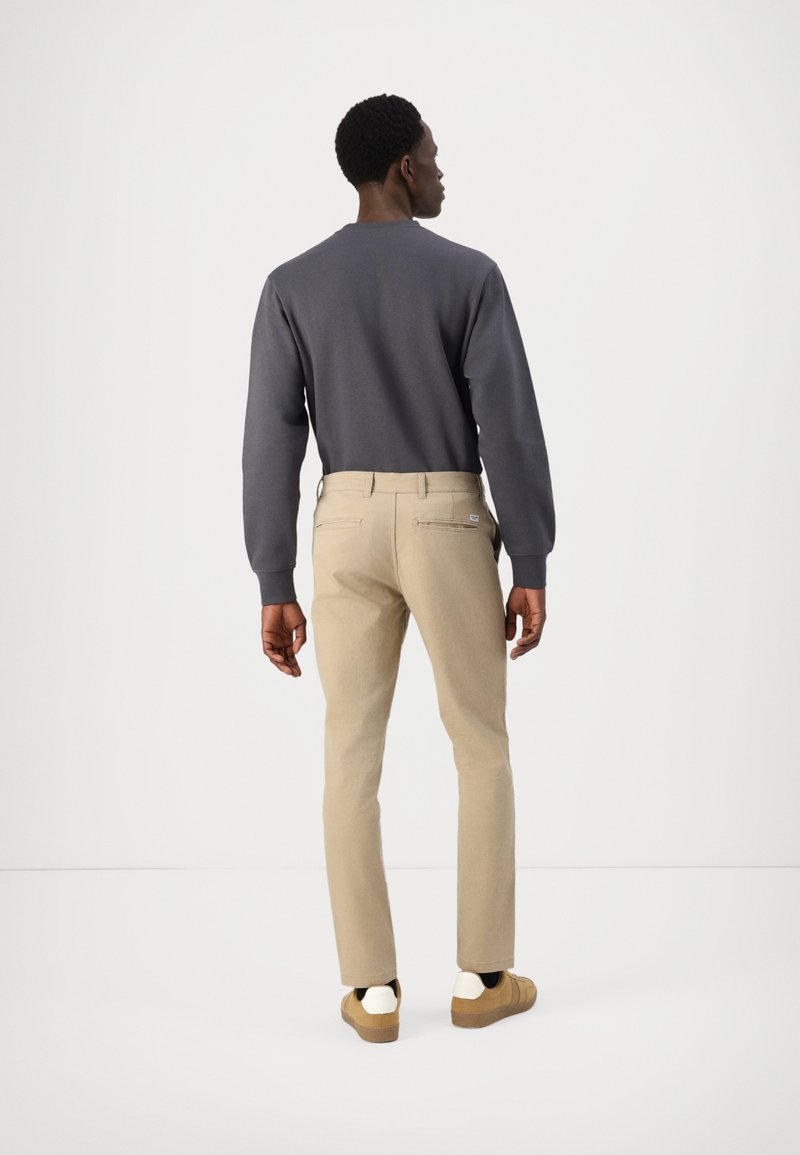 Felpa grigia a collo rotondo, pantaloni chinos slim-fit color khaki e sneakers beige senza lacci con dettagli bianchi, viste da dietro. Texture liscia.