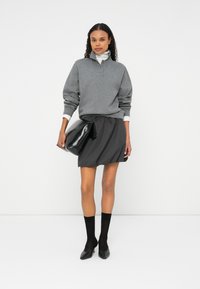 Szürke pulóver gallérral, sötétszürke redős szoknyával párosítva. Fekete kézitáska és bokáig érő zoknik hegyesorrú sarkakkal.