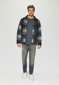 Herren-Flanellhemdjacke in marineblau, grau und cremefarbenem Karomuster, kombiniert mit einem grauen T-Shirt und hellgrauen Jeans; weiße Sneaker runden das Outfit ab.