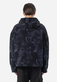 Svart fleece hettegenser med et strukturert, kamuflasjemønster. Har en romslig hette og avslappet passform, og viser frem det myke, plush stoffet.