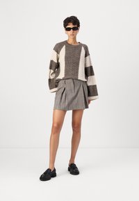 Chunky strikkegenser i brune og kremfargede striper, kombinert med et grått rutete plisseringskjørt. Brukt med svarte slip-on sko og solbriller.